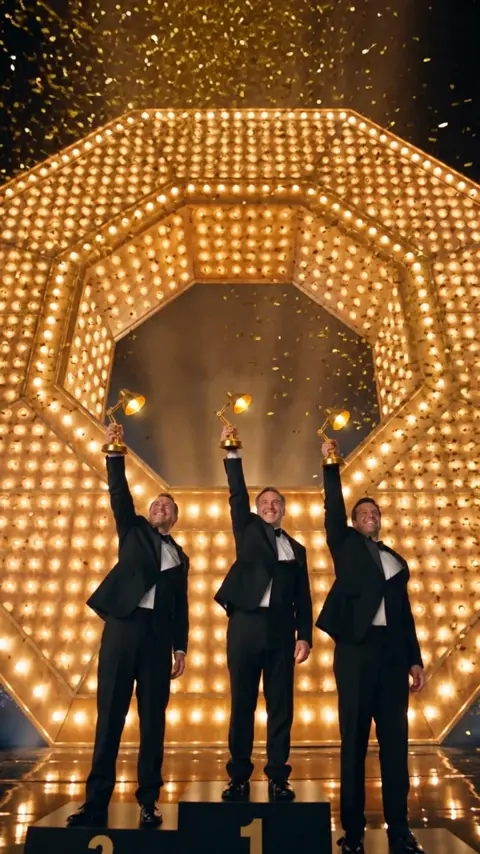The three winners on the podium raise their golden…